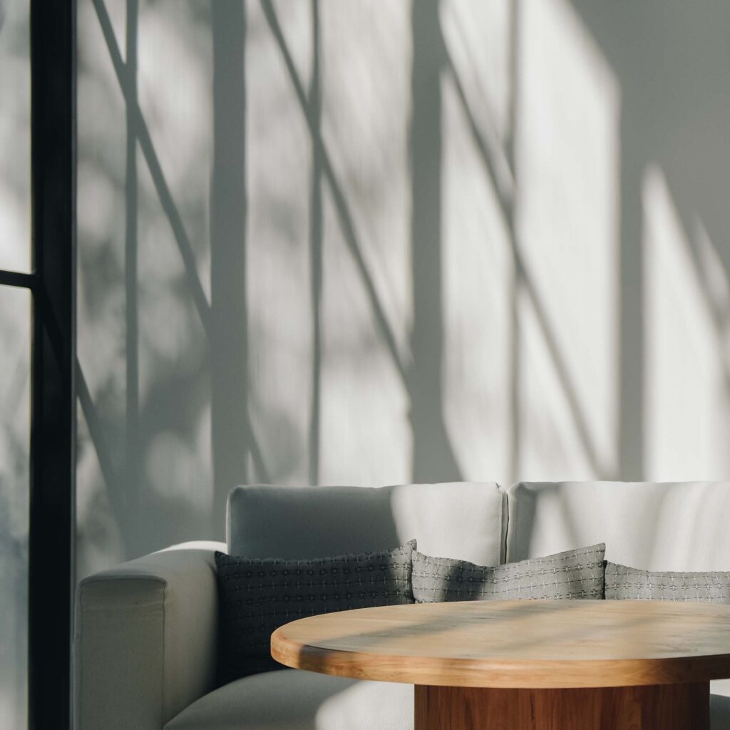 Minimalist living room with gray sofa and round wooden coffee table in natural sunlight.